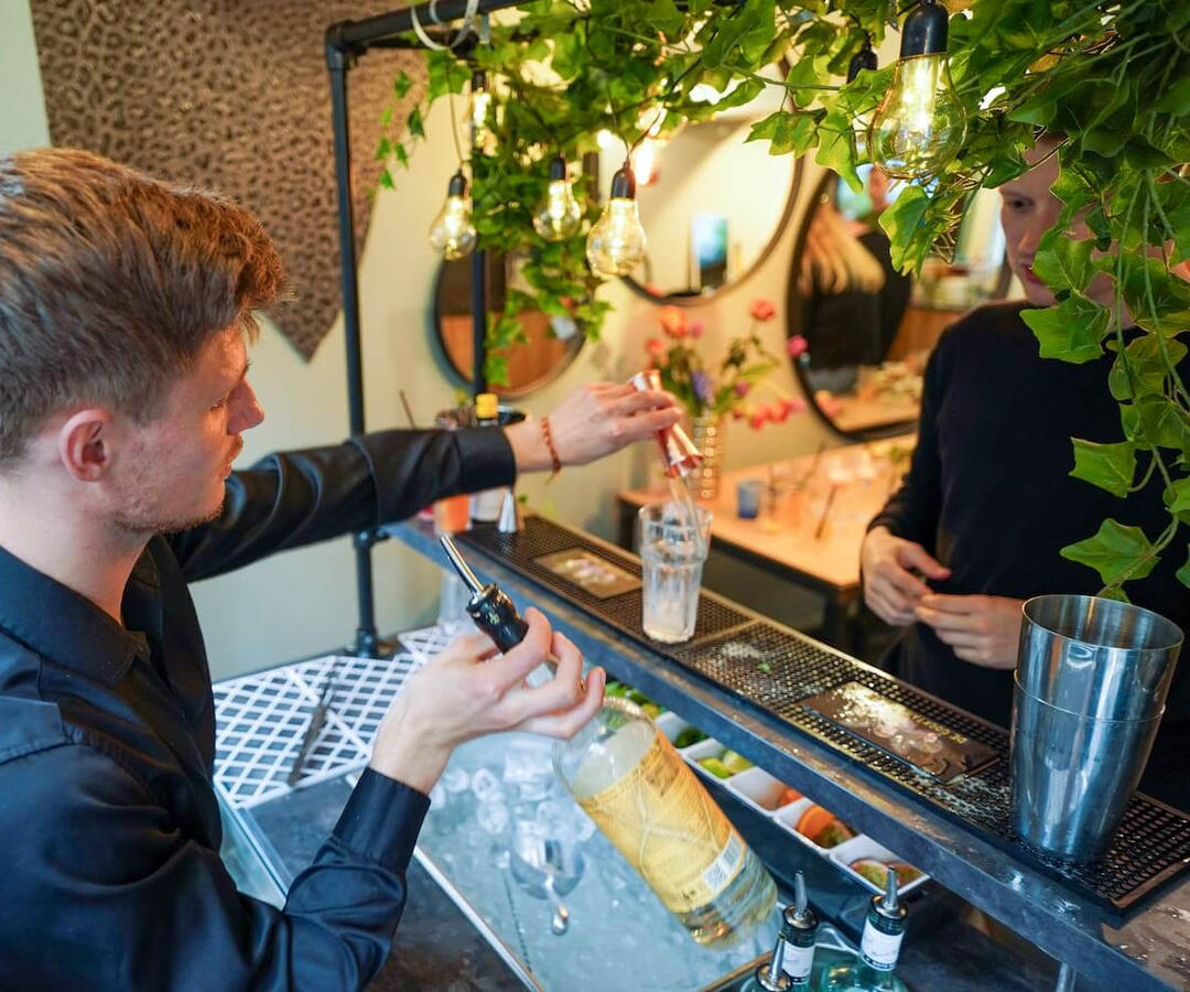 Cocktailshaker serveert een vers bereide cocktail aan een gast tijdens een feest in Rotterdam. Persoonlijke service en gastvrijheid bij mobiele cocktailbar op locatie in Zuid-Holland.