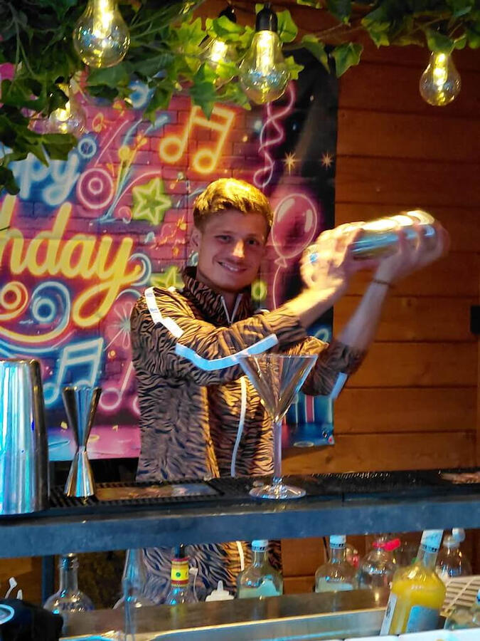 Cocktailshaker in retro jaren 80 outfit (fout pak) achter de mobiele bar tijdens een tuinfeest in Rotterdam Noord. Speciale service voor themafeesten en jaren 70/80 partijen in Zuid-Holland.